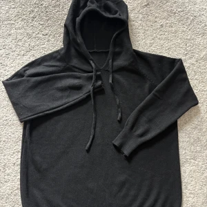 Svart stickad hoodie  - Svart hoodie med stickad känsla och mjukt material. Tröjan har långa ärmar, ribbade muddar och en stor huva med snörning framtill. Perfekt för dig som gillar enkel och clean stil. Passar dig som vill ha en chill och bekväm look. Lätt ”Kashmir hoodie” Grisch storlek Xs.