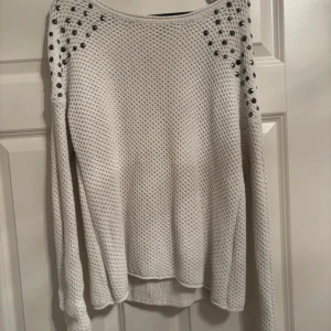 Vit stickad tröja med nitar från ONLY - Säljer en vit stickad tröja från ONLY i storlek L. Tröjan har lång ärm och är dekorerad med coola nitar och pärlor på axlarna för en edgy vibe. Perfekt för dig som vill sticka ut lite extra under höst och vinter.