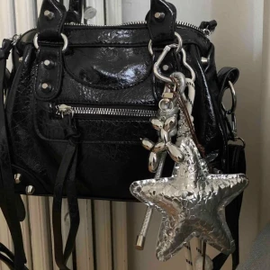 Silvrig stjärnformad väskdekoration - Cool accessoar till väskan med en silvrig stjärna i metallic-look, ballonghund i silver och detaljer med rep och hjärtformat spänne. 