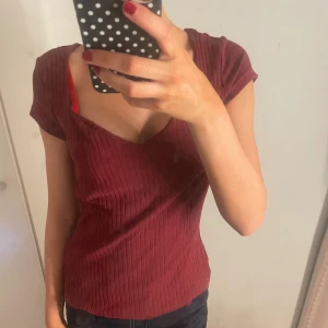 Vinröd Anna field - Säljer en vinröd ribbad topp med v-ringad hals och korta ärmar. Toppen har en slim passform och är tillverkad i mjukt, stretchigt material som sitter snyggt på 💋 Köpte för 400