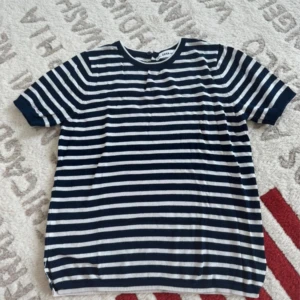 Randig stickad t-shirt från Zara - Säljer en stickad t-shirt från Zara i marinblått och vitt med klassiskt randigt mönster. T-shirten har korta ärmar, rund halsringning och liten slits i sidan. Perfekt för dig som gillar en chill och stilren look.