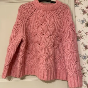 Rosa stickad tröja från H&M - Supermysig rosa stickad tröja från H&M med grovt kabelstickat mönster och hög krage. Tröjan har lång ärm och en loose fit som ger en chill vibe. Perfekt för kalla dagar! Köpt på Sellpy i nyskick