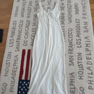 Vit långklänning med snörning XS - Supersnygg vit långklänning från Gina Tricot i storlek XS. Klänningen har v-ringad hals med snörning och fina spetsdetaljer längs kanterna. Axelbandslös design med smala band som knyts i ryggen. Mjuk och lätt polyester som ger en skön känsla.