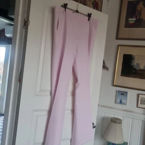 Ljusrosa bootcut byxor från BikBok - Snygga ljusrosa bootcut byxor från BikBok i storlek 42. Byxorna har hög midja, bälteshällor och diskreta fickor bak. Materialet är mjukt och har en lätt stretch för skön passform. Perfekt för dig som vill sticka ut med färg och stil.små i storleken. Passar L.