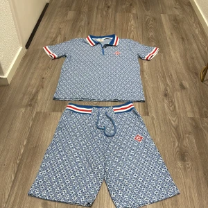 Blåmönstrade pike & shorts från Casablanca - Säljer ett par blå, vita, röda pike & shorts set från Casablanca med ett unikt geometriskt mönster. Shortsen har snörning i midjan och en elastisk linning med röd och vit rand. Materialet känns mjukt och passar perfekt till sommaren eller bara när du vill ta det chill. Storleken passar 164-176 pris kan diskuteras. 
