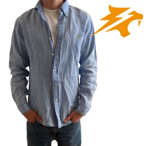 Ljusblå linneskjorta Ralph Lauren - Ljusblå skjorta från Ralph Lauren i slim fit med klassisk krage och knappar framtill. Tillverkad i svalt linne och har den ikoniska broderade loggan på bröstet. Perfekt för en clean och avslappnad look. En defekt i armhålan på höger sida. (se sista bilden)