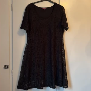Svart spetsklänning från Indiska - Svart kortklänning från Indiska i storlek L. Klänningen har ett vackert blommigt spetsmönster, rund halsringning och korta ärmar. Materialet är mjukt och följsamt, perfekt för dig som gillar en feminin och stilren look.