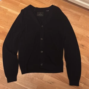 Mörk kofta från Jack & Jones premium kollektion  - Stilren mörkblå kofta från Jack & Jones Premium med v-ringad hals och knappar framtill. Långärmad modell i mjuk bomull som passar perfekt till lager-på-lager. Enkel design utan mönster, vilket gör den lätt att matcha med olika outfits. Nypris 900kr