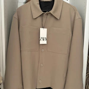 Beige jacka från Zara - Stilren oanvänd (prislapparna kvar) beige jacka från Zara i ordentligt material i storlek S. Jackan har två stora bröstfickor, klassisk krage och knäppning med fyra knappar framtill. Perfekt för lager-på-lager och har en clean, minimalistisk look som funkar till många stilar.