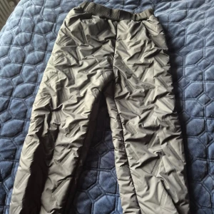 Svarta täckbyxor med mönster, strl 130 - Säljer ett par svarta täckbyxor med coolt strukturerat mönster och mjukt vitt fleecefoder på insidan. Byxorna har resår i midjan för skön passform och är perfekta för kalla dagar. Snyggt och funktionellt plagg för dig som gillar att vara ute även när det är kallt.