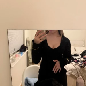 Svart långärmad tröja med v-ringning - Säljer en svart, figurnära stickad tröja med lång ärm och djup v-ringning. Har en enkel och stilren design som framhäver siluetten. Perfekt för dig som gillar en klassisk look med en touch av edge.