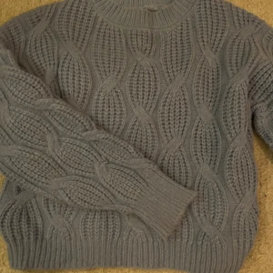 Blå stickad tröja med flätmönster - Säljer en blå stickad tröja med snyggt flätmönster och rund hals. Tröjan har långa ärmar och breda muddar vid ärmslut och nederkant. Perfekt för kyliga dagar och riktigt mysig att ha på sig.