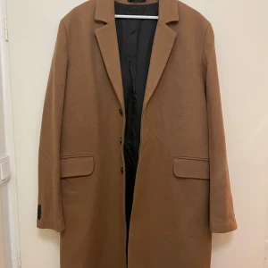 Brun Rock - Oanvänd brun rock från Weekday i klassisk rak modell med krage och knappar framtill. Jackan har två fickor med lock och är helfodrad med svart tyg. Strlk 52/Large