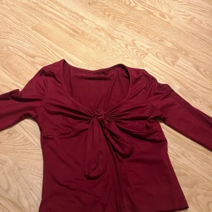 Vinröd omlottopp med knyt - Säljer en vinröd omlottopp med knyt framtill och v-ringad hals. 