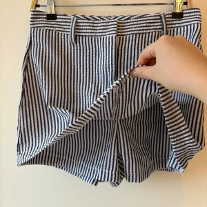 Randiga blåvita skort - Snygga skort (kjol med shorts / innerbyxa) med blå och vita vertikala ränder, klassisk midja och praktiska fickor fram. De har hällor för bälte och är gjorda i ett lätt och luftigt bomullstyg, perfekt för varma dagar. Passformen är normal och stilen är tidlös med en fräsch vibe. Står strl L, men passar en liten M / stor S. endast testad aldrig använd 