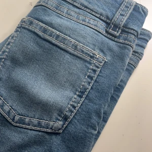 Blå bootcut jeans från Ginatricot - Snygga blå jeans från Ginatricot i storlek 158. Klassisk femficksmodell med vita kontrastsömmar och dubbla knappar i midjan. Jeansen har bootcut-ben och är tillverkade i mjukt denimtyg som sitter skönt hela dagen.