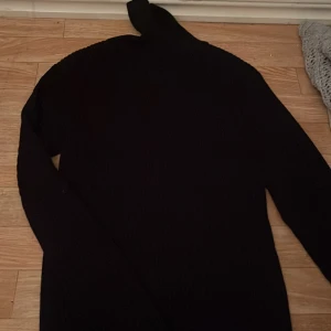 Svart ribbad polotröja från Pop England - Svart polotröja från Pop England i storlek M. Tröjan är ribbstickad med lång ärm och har en klassisk hög polokrage. Perfekt för dig som gillar stilrena och enkla plagg med snygg passform. Materialet känns mjukt och stretchigt.