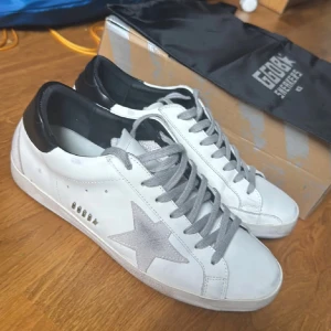 Golden Goose vita sneakers med stjärna - Golden Goose sneakers i vitt skinn med grå snörning och silverfärgad stjärndetalj på sidan. Hälpartiet är svart och sulan är platt. Bra skick 9/10 endast använda ett fåtal gånger, box samt dustbag medförljer.