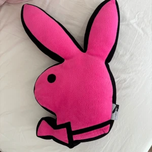 Playboy Home kudde - Unik Playboy Home kudde i form av den ikoniska kaninen, tillverkad i mjuk rosa polyester. Designad 2008, i fint skick utan synligt slitage. Perfekt som dekor eller present till samlare och fans av varumärket.