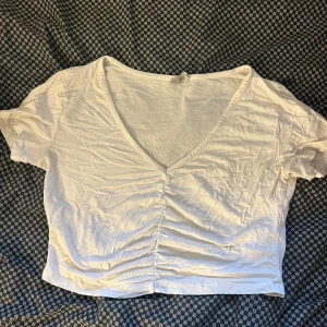 Vit croppad topp med snörning från ASOS - Säljer en vit croppad topp från ASOS med snygg v-ringning och snörning framtill som ger en cool rynkad effekt. Toppen har korta ärmar och är gjord i mjuk bomull, perfekt för att styla med jeans eller kjol. Enkel och fräsch design som funkar året runt.