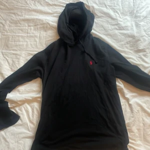 Svart hoodie från Polo Ralph Lauren - Svart hoodie från Polo Ralph Lauren med klassisk röd broderad logga på bröstet. Tröjan har huva med snörning och långa ärmar. Tillverkad i mjuk bomull som är skön mot huden. Den är i mycket bra skick och inte användts så ofta! Pris kan diskuteras vid snabb affär!