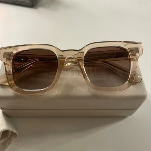 Beige CHIMI solglasögon i fyrkantig modell - Snygga solglasögon från CHIMI med transparent beige båge och fyrkantig form. Glasen är bruna med en mjuk toning. Kommer med originalfodral och putsduk. Perfekt accessoar för att lyfta din stil. Nyskick 1400kr
