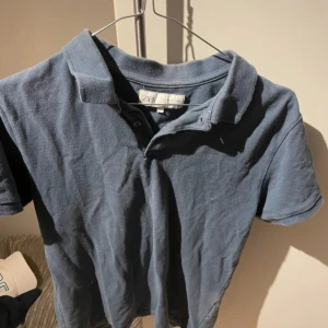 Blå pikétröja från Zara - Snygg blå pikétröja från Zara med klassisk krage och korta ärmar. Tröjan har knappar vid halsen och är tillverkad i mjuk bomull som är skön mot huden. Perfekt för dig som gillar enkel och stilren look.