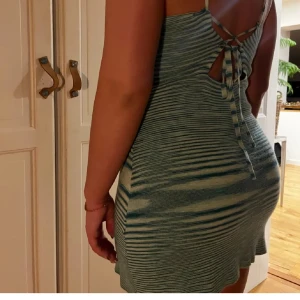 Randig blågrön kort klänning med snörning - Superfin kort klänning med tunna axelband och snygg snörning i ryggen. Klänningen har ett randigt mönster i blått och beige, och är figurnära med en tight passform. Perfekt för dig som gillar en unik och trendig look.