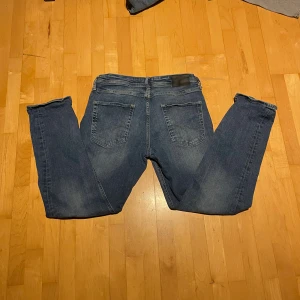 Blå tapered Jack and jones jeans Mike 31/30 - Säljer ett par blå jeans från Mike i modellen Tapered. Jeansen har klassisk femficksdesign, gul kontrastsöm och en snygg tvätt med lätt slitning. Passformen är tapered vilket ger en modern siluett som smalnar av mot ankeln. Perfekt för dig som gillar stilrena jeans.