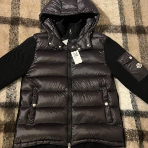 Moncler cardigan - Otroligt snygg🙌Maglione Tricot Cardigan  från Moncler i svart färg, storlek L/3 men passar M. Jackan är i riktigt fint skick och passar perfekt både till vardags😁 och kyligare kvällar❄️. Modellen heter Maglione Tricot Cardigan❗️, en av Monclers mest populära hybridplagg som kombinerar lätt dunväst framtill med stickade ärmar i premium bomull/ull🐑Denna cardigan köptes på Vinted med ❗️artikel verfering❗️och man får med vinted taggen! Men är gott som ny för den inte har använts,🛍️ Kontakta mig✅