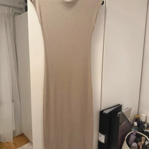 Beige långklänning från Nelly - En stilren beige långklänning från Nelly i storlek S. Klänningen har en rak och tight passform med ärmlös design och rund halsringning. Materialet är mjukt och stretchigt, perfekt för en clean och minimalistisk look.