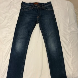 Mörkblå slim jeans Jack & Jones - Snygga mörkblå slimjeans från Jack & Jones i storlek 28/32. Klassisk femficksmodell med kontrastsömmar och läderpatch bak. Jeansen har en smal passform och är tillverkade i stretchigt denim för extra komfort.