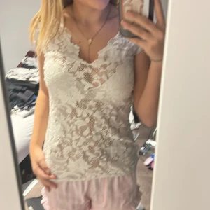 Vit spetsblus med v-ringning - Säljer en vit blus i spets med v-ringad hals och korta ärmar. Blusen har ett blommigt spetsmönster och är lätt transparent, vilket ger en romantisk och fräsch vibe. Perfekt för dig som gillar detaljer och vill ha något som sticker ut lite extra.