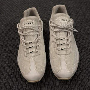 Nike Air Max 95 vita sneakers - Säljer ett par Nike Air Max 95 i helvitt med svarta detaljer. Skorna har mesh och syntetpaneler, synlig Air Max-dämpning i sulan och klassisk snörning. Diskret Air Max- och Nike-logga på sidor, plös och häl. Perfekta för dig som gillar stilrena sneakers.