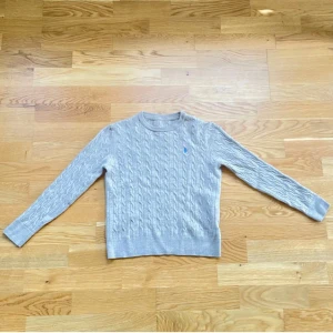 Beige kabelstickad tröja från Morris - Snygg beige kabelstickad tröja från Morris med rund hals och lång ärm. Diskret blå logga broderad på bröstet. Perfekt för dig som gillar klassisk stil med en modern touch. Den sitter tajtare än andra Morris tröjor fast är riktigt snygg. Den passar för 140-145 och priset kan diskuteras. 