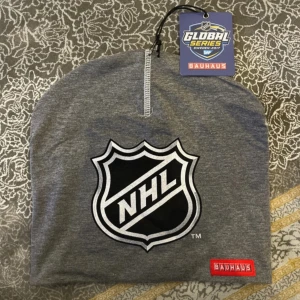Grå NHL mössa från Bauhaus - Snygg grå mössa med stort NHL-logga framtill och Bauhaus-märke. Perfekt för hockeyfans som vill visa sin stil. Mjuk och skön passform, tillverkad i bomullsmaterial. Tagg från Global Series Sweden 2017 medföljer.