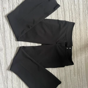 Svarta kostymbyxor Gina Tricot M - Snygga svarta kostymbyxor från Gina Tricot i storlek M. Byxorna har en flare figur, låg midja och stängs med dragkedja, hake och knapp. Materialet är mjukt och har en lätt stretch. Perfekt för en clean och stilren look. Varan är väldigt ny och är bara använd ett fåtal gånger men har ett uppskrapat skrubbsår men det är ej ett hål som syns. (Se bild)