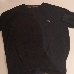 Mörkblå stickad tröja från Gant - Snygg mörkblå stickad tröja från Gant med diskret logga broderad på bröstet. Tröjan har rund halsringning och långa ärmar, perfekt för kyligare dagar. Klassisk och stilren modell som passar till det mesta.