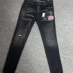 Svarta skinny jeans från Dsquared2 - Snygga svarta jeans från Dsquared2 med skinny passform och slitna detaljer. Jeansen har en broderad patch med DSQ2 1964 på framsidan och en stor Dsquared2-label bak i midjan. Materialet är klassisk jeans och färgen är mörk med tvättade effekter.
