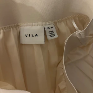 Plisserad beige långkjol från VILA - Säljer en superfin plisserad långkjol från VILA i en ljus beige nyans. Kjolen har bred resår i midjan och ett snyggt fall med tydliga veck. Perfekt för dig som gillar en stilren och elegant look.