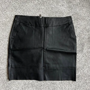 Svart skinnkjol - 🤍 Svart kort skinnkjol från ONLY i storlek 38. Kjolen har en rak passform och en synlig dragkedja bak 🤍