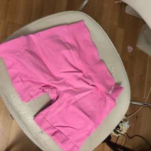 Rosa träningstights shorts från DFYNE - Säljer ett par korta, tighta träningstights i en snygg rosa färg från DFYNE. De har hög midja med bred resår och är tillverkade i ett stretchigt material som sitter skönt på kroppen. Perfekta för gymmet eller löprundan.