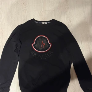 Svart sweatshirt från Moncler - Moncler tröja i storlek L, nästan som ny har bara använt den ett få tal gånger. Har två små öppningar på ena armen, men de går enkelt att sy och syns knappt när tröjan används.
