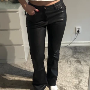 Svarta bootcut byxor i skinnimitation - Snygga svarta byxor i skinnimitation med bootcut passform. Perfekt för dig som vill ha en edgy och trendig look.