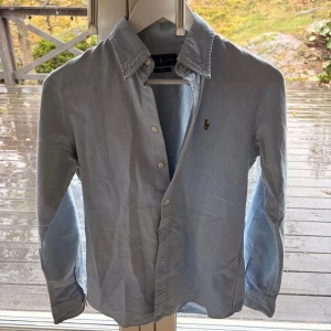 Ljusblå skjorta från Ralph Lauren - Snygg ljusblå skjorta från Ralph Lauren i bomull, custom fit, är 173 och den passar perfekt. Klassisk krage, långa ärmar och knappar framtill. Ikoniska broderade loggan på bröstet ger en clean och stilren vibe. Perfekt för dig som gillar tidlös stil och vill ha något som funkar till jeans eller chinos. Nypris 1600kr 