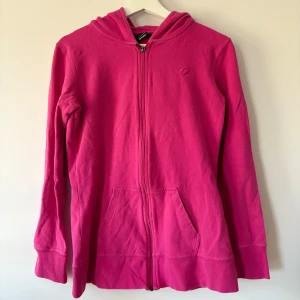 Rosa hoodie från SOC med dragkedja - Snygg rosa hoodie från SOC i storlek 38. Tröjan har huva, hel dragkedja framtill och två praktiska fickor. Tillverkad i mjuk bomull som är skön att ha på sig. Perfekt för chill dagar eller när du vill ha en färgklick i garderoben.