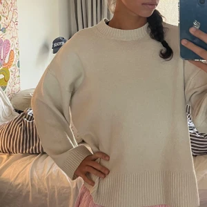 Cremevit oversized stickad tröja - Säljer en beige oversized stickad tröja med breda ribbade muddar vid ärmslut och nederkant. Tröjan har en rund halsringning och långa ärmar, perfekt för lager-på-lager och chill dagar.