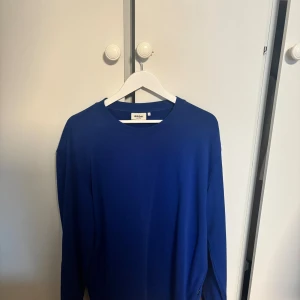Blå långärmad tröja från Dobber - En stilren blå långärmad tröja från Dobber med rund hals och enkel design. Perfekt för dig som gillar cleana och klassiska plagg. Materialet känns mjukt och skönt mot huden, och passformen är normal. Snygg att matcha med jeans eller chinos.