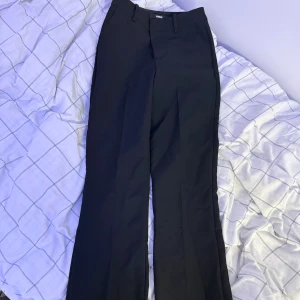 Svarta kostymbyxor från Bik Bok - Snygga svarta kostymbyxor från Bik Bok i klassisk rak modell med pressveck. Byxorna har hällor för bälte, sidfickor och stängs med dragkedja och knappar. Perfekta för en clean och stilren look.