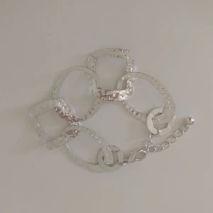 Silvrigt armband med stora länkar - Stilrent armband i silverfärgad metall med stora, hamrade länkar i både rund och fyrkantig form. Länkarna ger ett coolt och modernt uttryck och armbandet har justerbar kedja med lås. Perfekt för dig som gillar statement-smycken och vill sticka ut.
